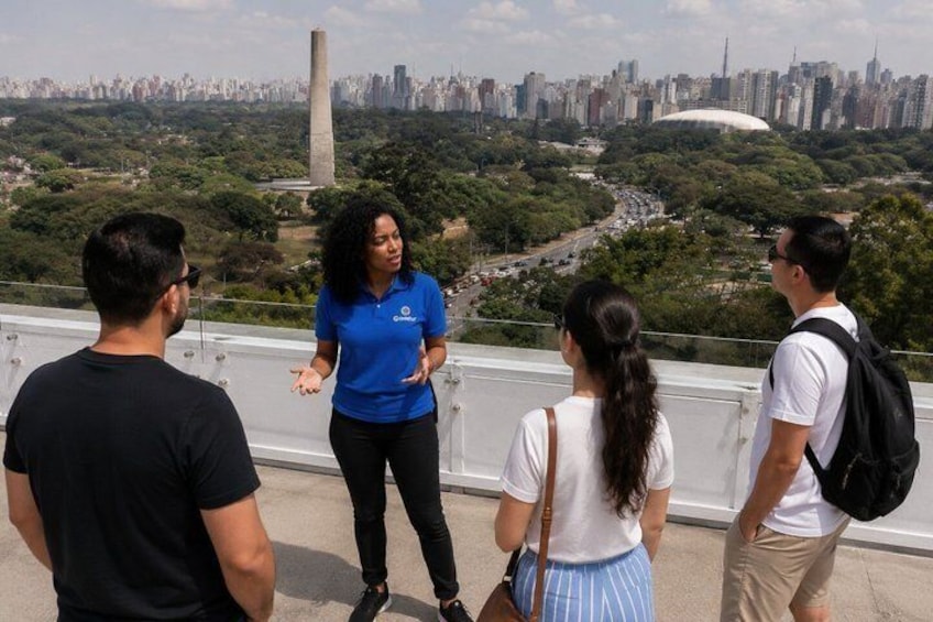 A group of people standing on a viewing platform overlooking a cityscape with a prominent monument and a stadium. 2
