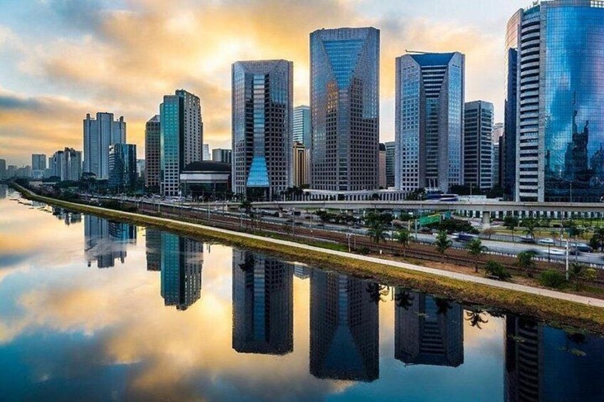 A city skyline with modern skyscrapers, a river reflecting the buildings, and a clear sky. 2