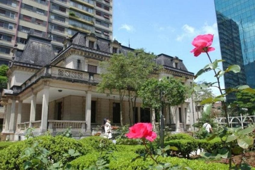 Un bâtiment historique doté d’un jardin, une rose rose et, en arrière-plan, un immeuble moderne de grande hauteur. 2