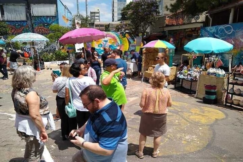 Un marché animé, où les gens font leurs courses et où les vendeurs proposent leurs produits sous des parasols colorés. 1