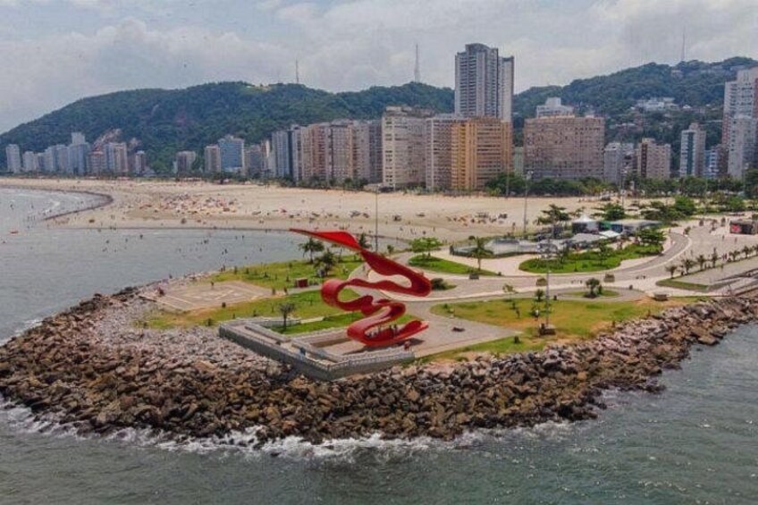 Een kuststadsgezicht met een opvallende rode sculptuur, een strand en hoge wolkenkrabbers. 3