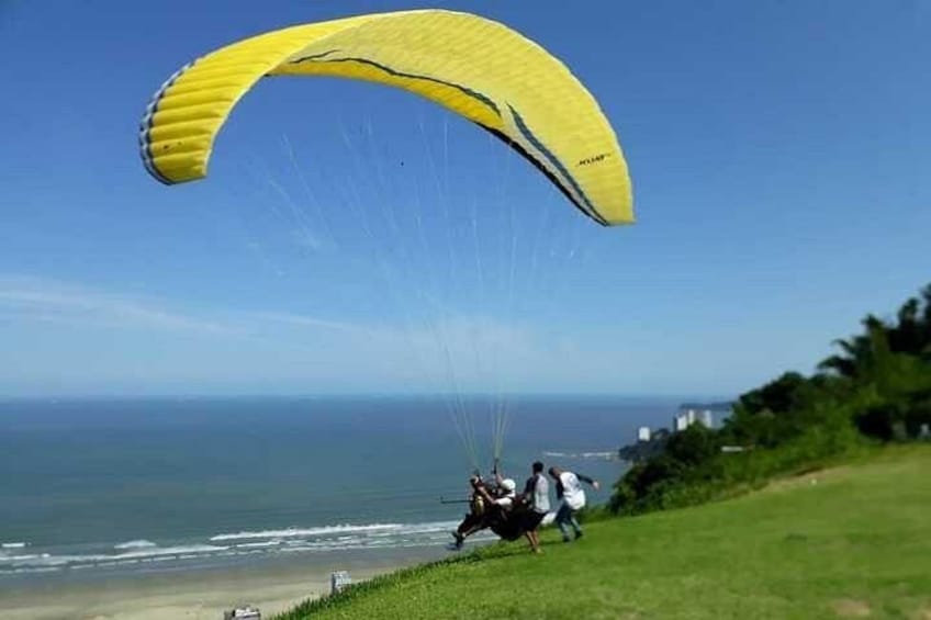 Een persoon paraglidet boven een kustlandschap met een gele vlieger. 2