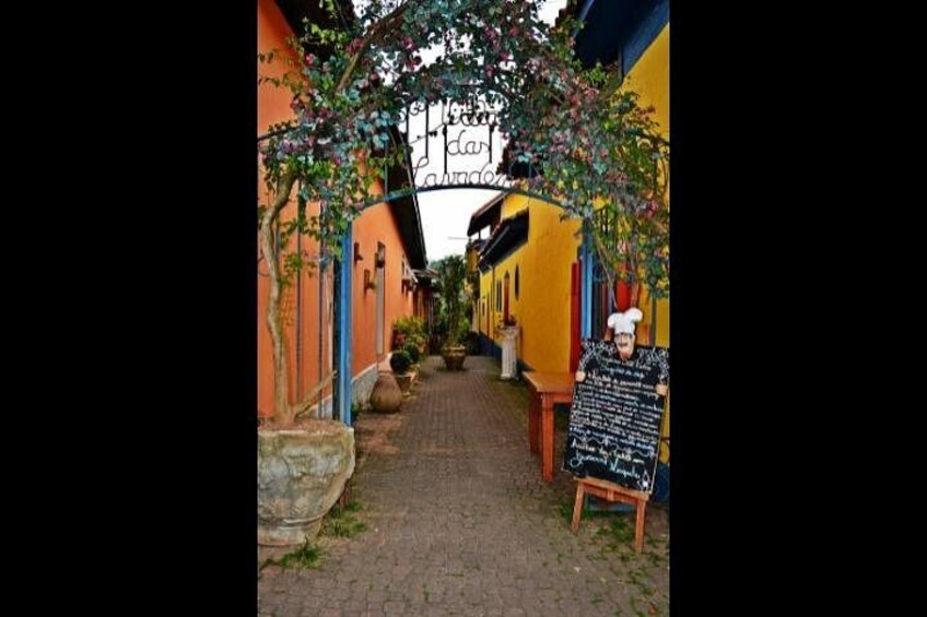 A narrow alleyway with yellow buildings, a stone bench, and a chalkboard sign. 2