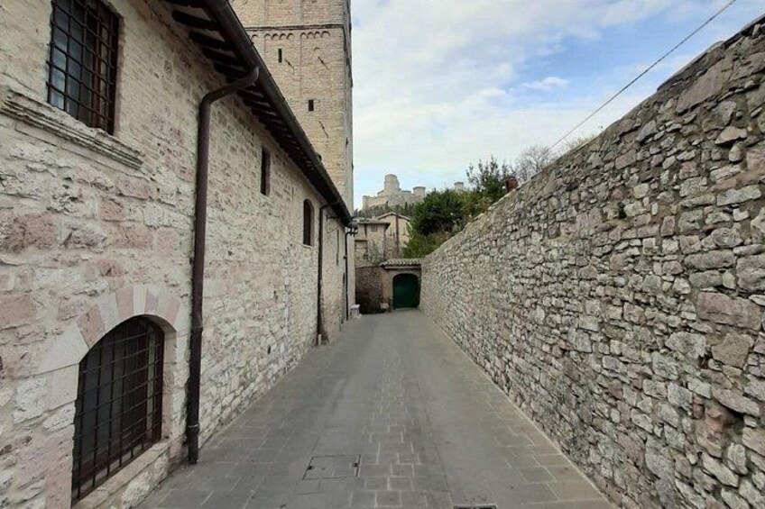 A narrow alleyway flanked by stone walls and buildings with arched windows. 5
