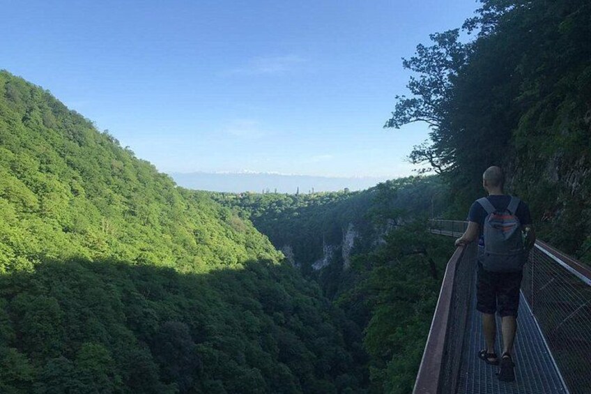 Eine Person geht über eine Hängebrücke über ein üppiges, grünes Tal. 3
