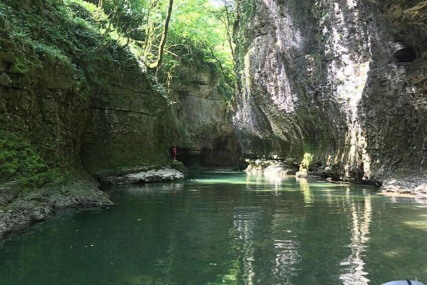Eine natürliche Höhle mit einem Wasserbecken, umgeben von felsigen Klippen und viel Grün. 2