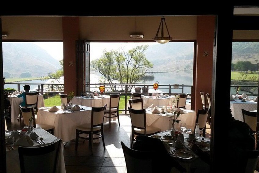 An outdoor dining area with tables set for a meal, overlooking a lake and mountains. 2