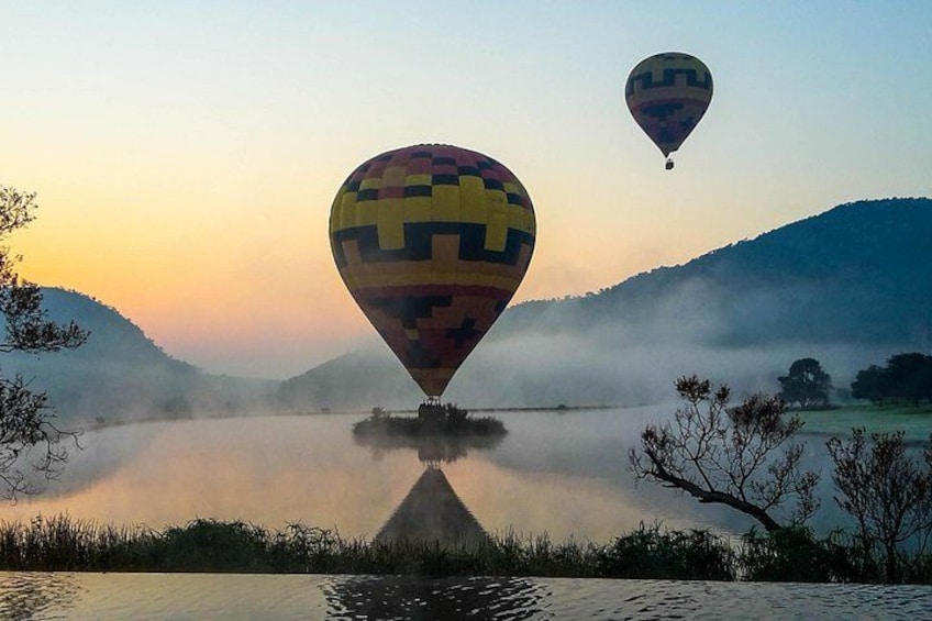Two hot air balloons over a calm lake with mist and hills in the background. 3