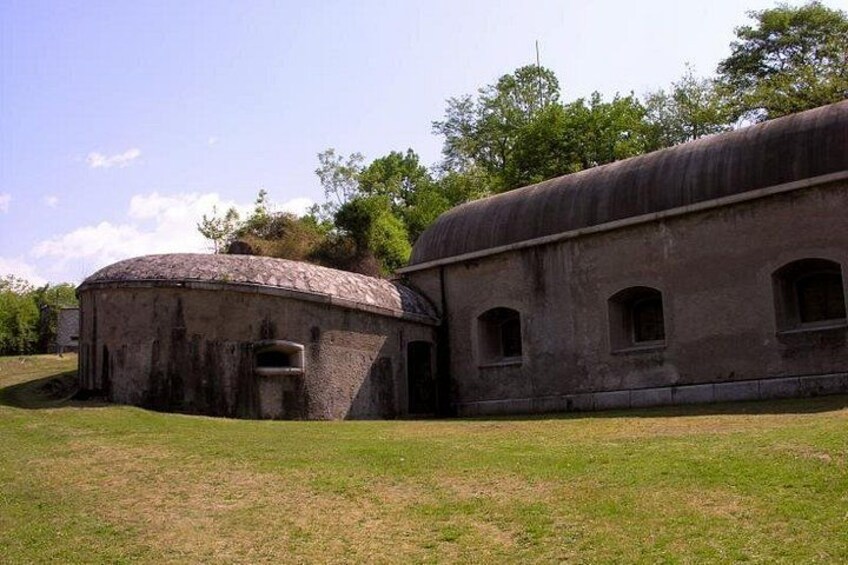 A large, circular building with a dome roof, a rectangular building with arched windows, and a grassy field in the foreground. 2