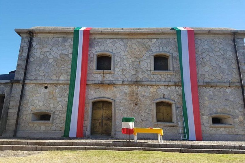 Edificio de piedra con dos ventanas arqueadas y una puerta, decorado con una bandera. 5