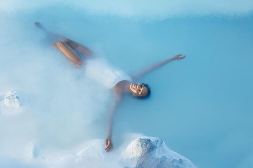 A person floating in a clear blue pool with a snowy mountain in the background. 1