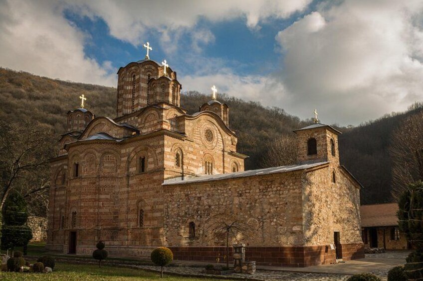 Une église en pierre, dotée de plusieurs coupoles et de croix, entourée d’un paysage vallonné. 1