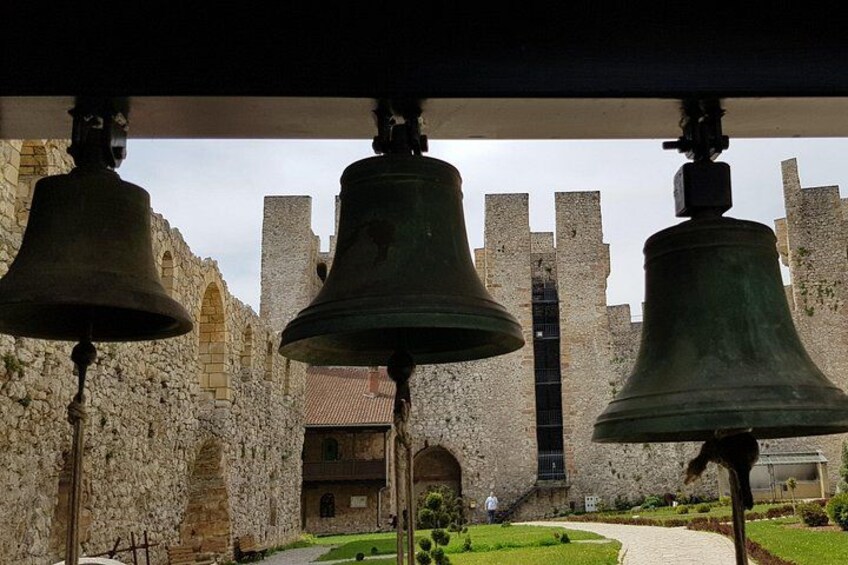 Trois grandes cloches sont suspendues devant un bâtiment historique en pierre, doté d’une tour. 3