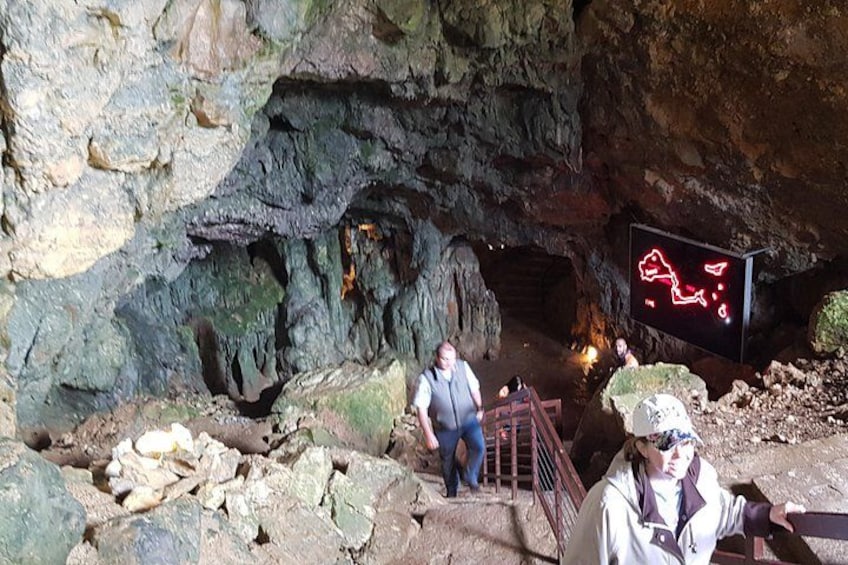 A cave entrance with a wooden staircase leading down, a neon sign, and rocky walls. 3