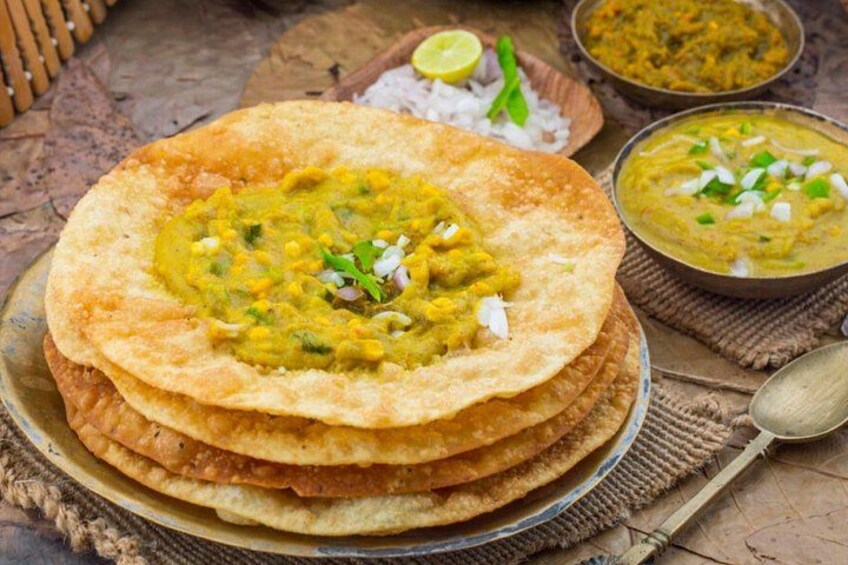 Een stapel platbroden met groene curry erover, vergezeld van kommetjes curry en een lepel op een rustieke tafel. 1