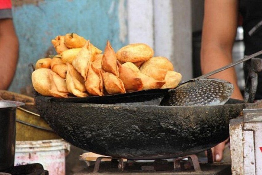Een zwarte pan met goudbruine gefrituurde hapjes, waarschijnlijk samosa's, op een kookplaat. 3