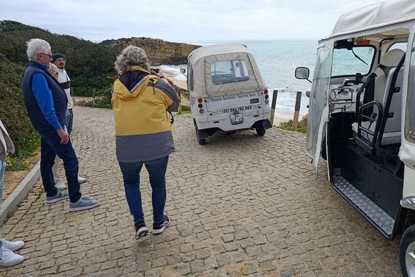 A group of people standing near a vehicle on a cobblestone path by the sea. 2