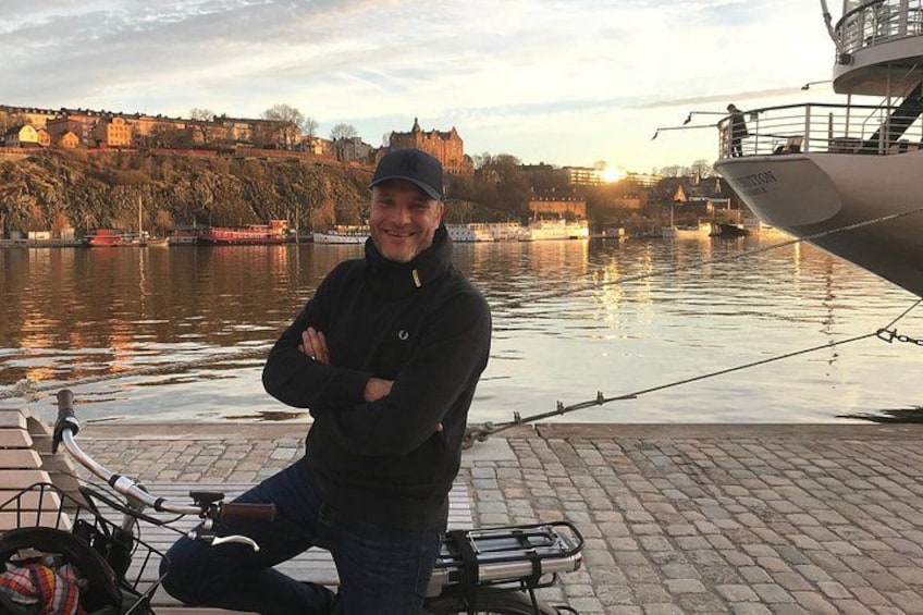 Una persona sentada en un muelle con una bicicleta, un barco y un castillo al fondo. 4