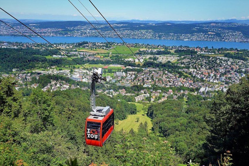 A red cable car with 'I love you' written on it, suspended above a lush green landscape with a town in the background. 1