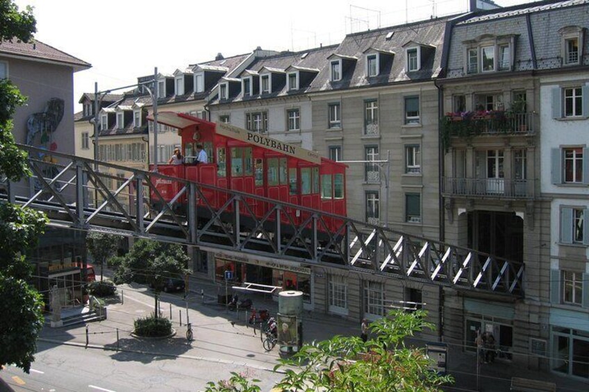 A red tram on a bridge, buildings, and a pedestrian walkway. 1