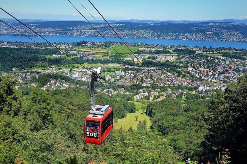 Un teleférico rojo con el texto 'I ♥ YOU', suspendido sobre un paisaje verde exuberante con un pueblo abajo. 1