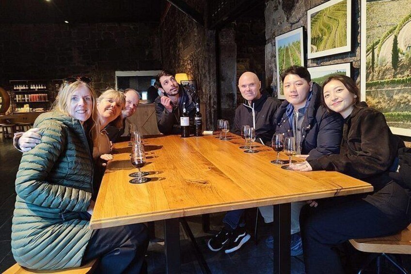 A group of people seated around a wooden table with wine glasses and bottles. 5