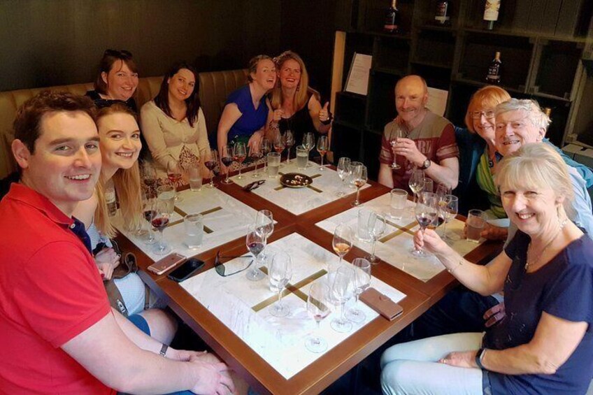 A group of people seated around a table with wine glasses and plates, suggesting a social gathering or meal. 2