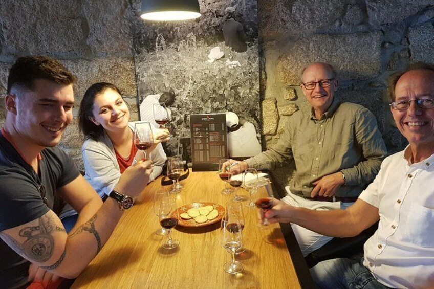 A group of people sitting around a wooden table with wine glasses, a bottle, and a bread basket. 1