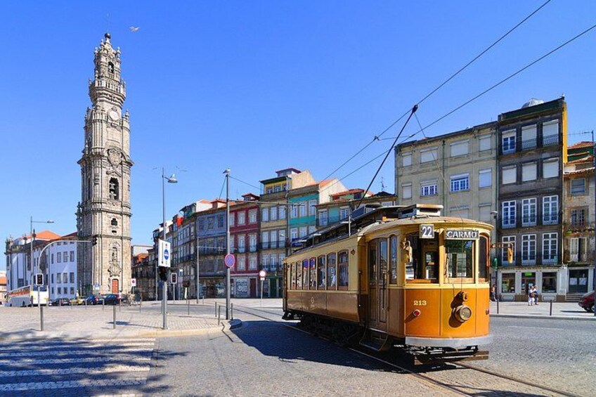 A yellow tram on tracks, a historic tower, and colorful buildings. 1