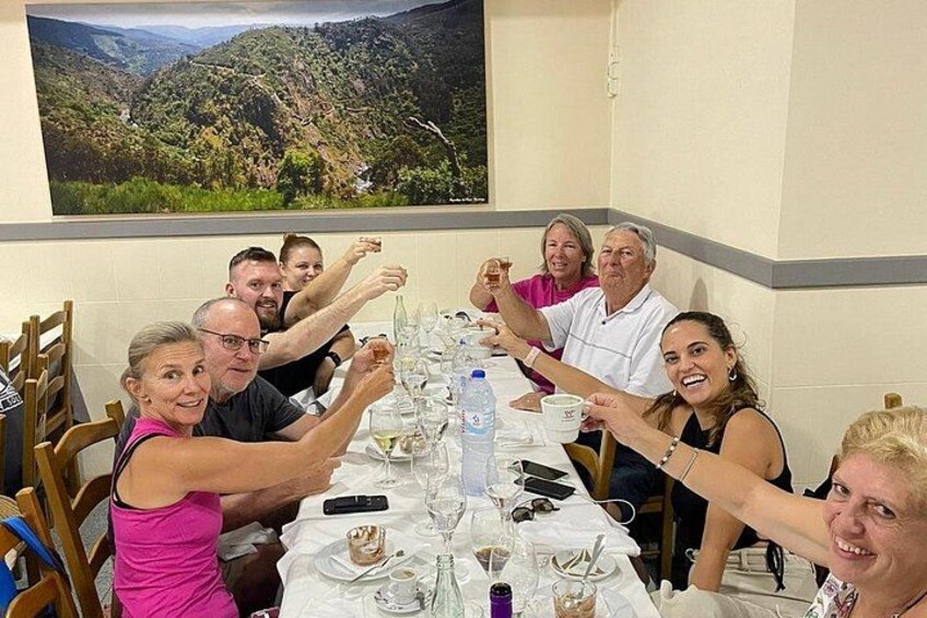Un grupo de personas brindando alrededor de una mesa, con una pintura de paisaje al fondo. 1