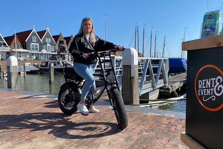 A person on a stationary bike near a waterfront with boats and buildings in the background. 3