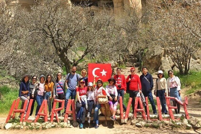 A group of people posing in front of a sign with the word "HALAVALE" and a Turkish flag. 1