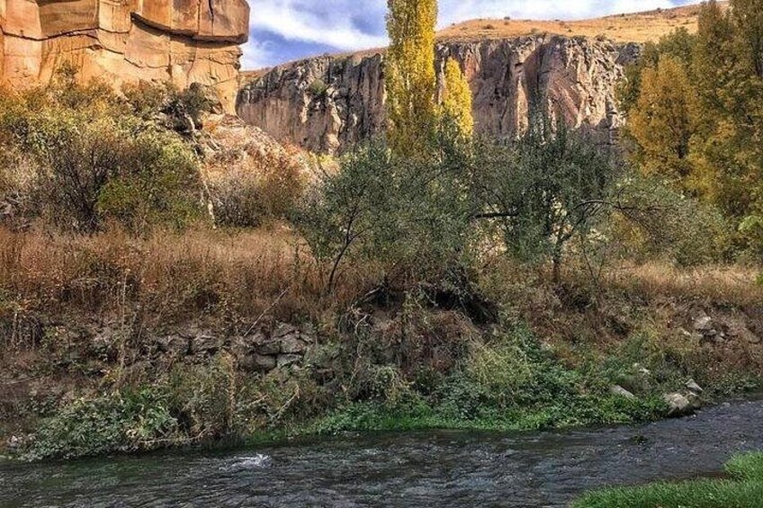 A river flowing through a rocky landscape with sparse vegetation and a cliff in the background. 2