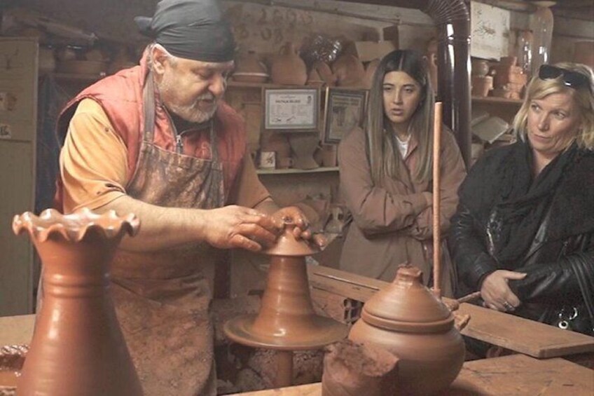 A pottery workshop with a potter shaping clay on a wheel, surrounded by pottery tools and unfinished pots. 3