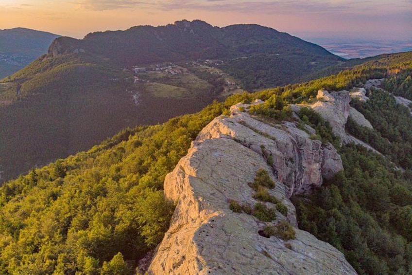 A mountainous landscape with a rocky outcrop and dense forest. 1