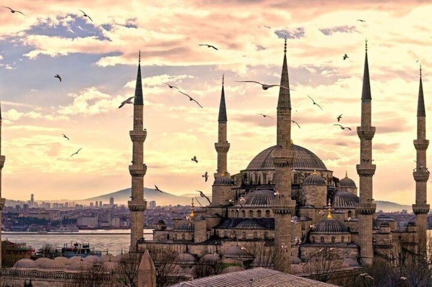 Una mezquita histórica con varios minaretes y cúpulas, rodeada por un paisaje urbano y un río. 5