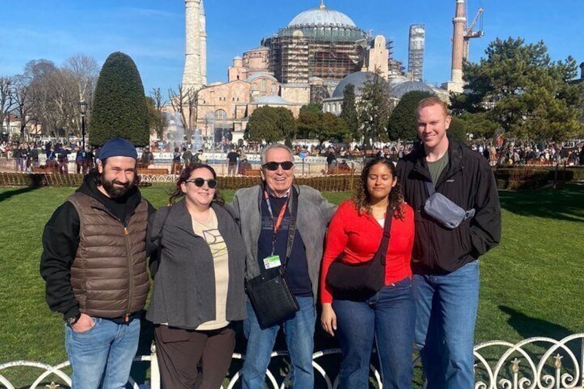 A group of people standing in a park with a historic building in the background. 5