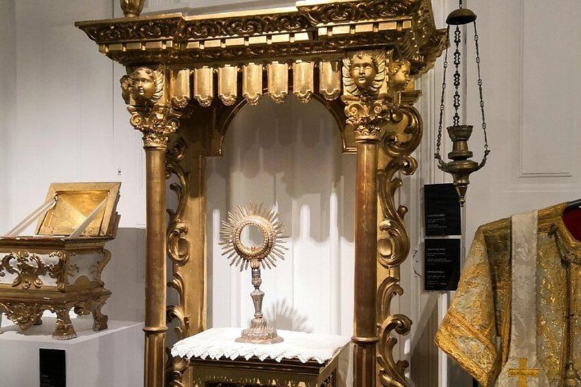 En gylden, detaljeret religiøs bygning med et centralt alter, et indrammet billede og en hængende lampe. 3