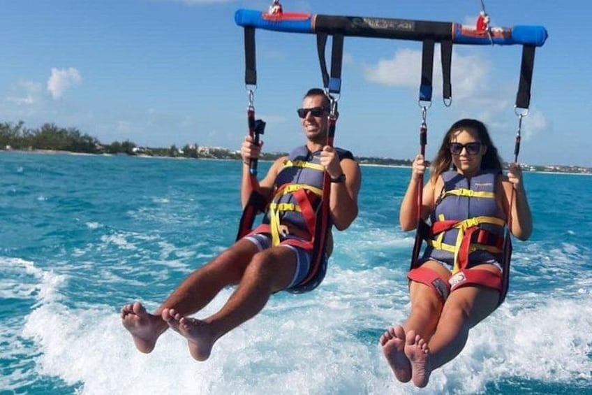 Two people on a water sport activity, wearing life jackets and holding onto a bar. 1