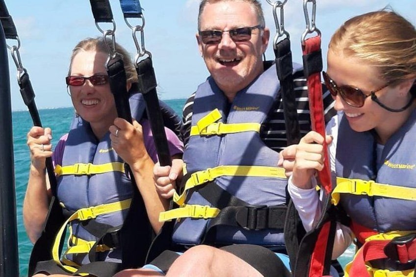 Three people in blue life jackets with yellow stripes, holding onto harnesses on a boat. 2