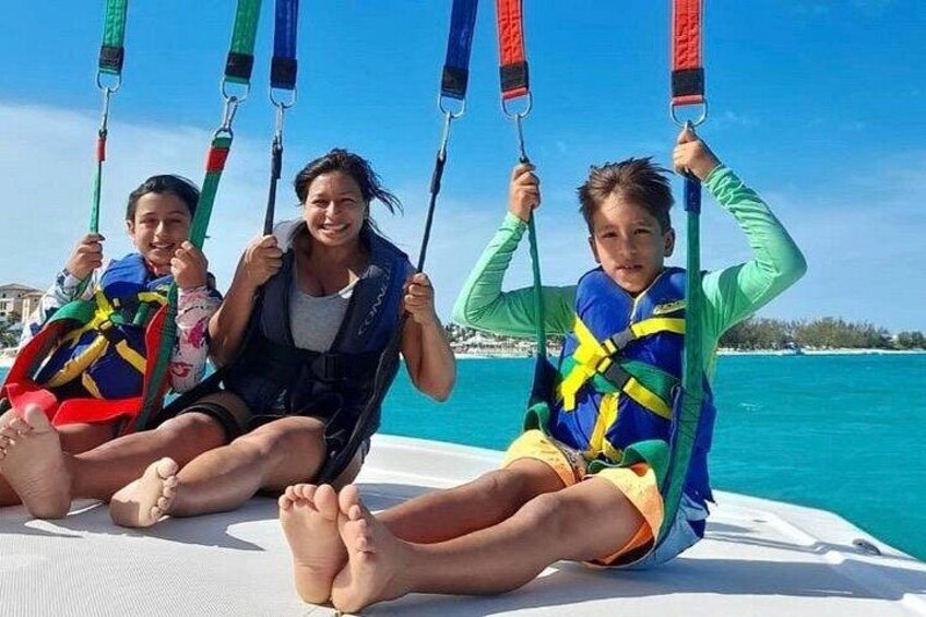 Three people sitting on a boat with life jackets, holding onto ropes. 2
