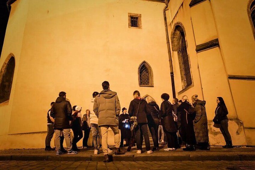 A group of people standing in front of a building with a pointed arch window. 5
