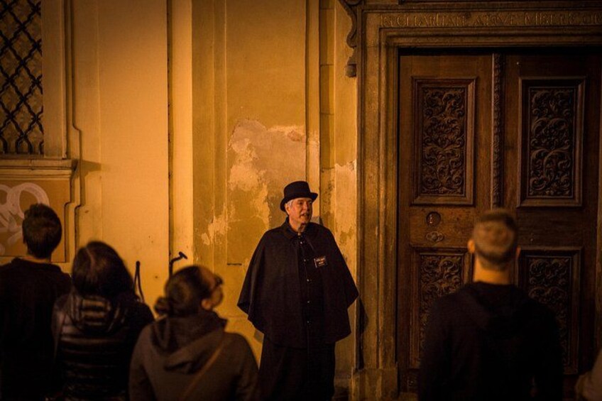 A person in a dark robe standing in front of a group of people, with a large ornate door in the background. 3