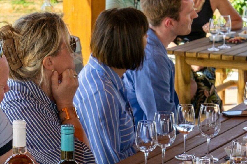 Menschen sitzen an einem Holztisch, Wein gläser und Flaschen stehen bereit. 3