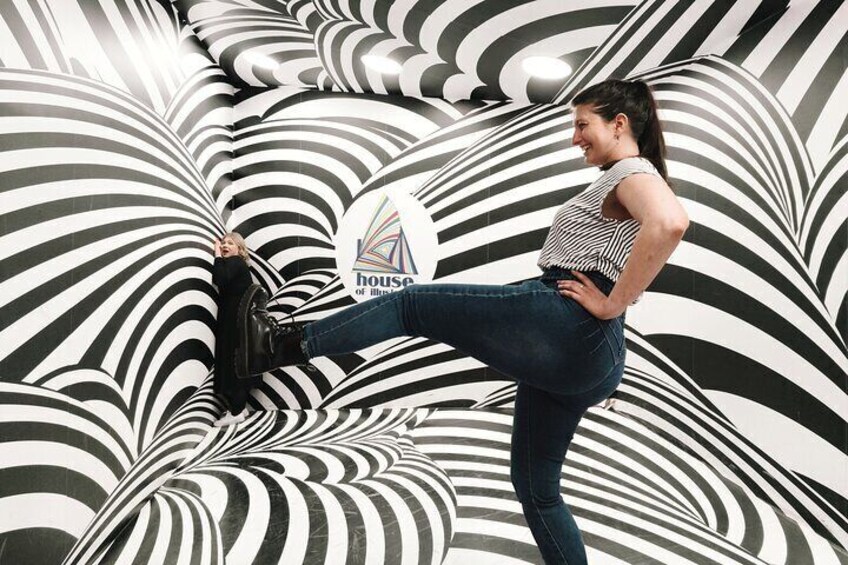 A person in a striped top and jeans standing on a patterned floor with a logo in the background. 4