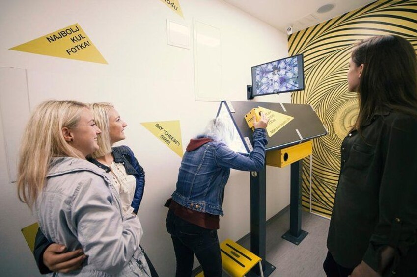 A group of people interacting with a touchscreen display in a room with geometric wall patterns. 2