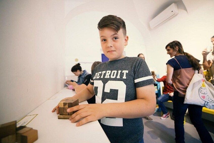 A child holding a wooden block, wearing a Detroit sports jersey, in a room with white walls and a visible air conditioning unit. 2