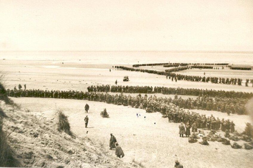 A beach with a large crowd gathered in the middle, a few people walking along the shore, and a distant pier. 2