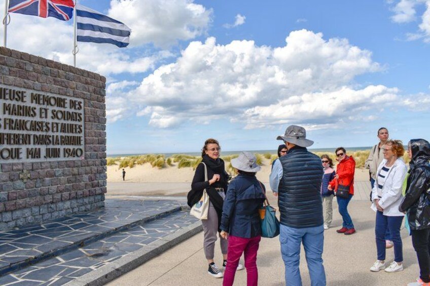 A group of people standing near a wall with a plaque and flags. 4
