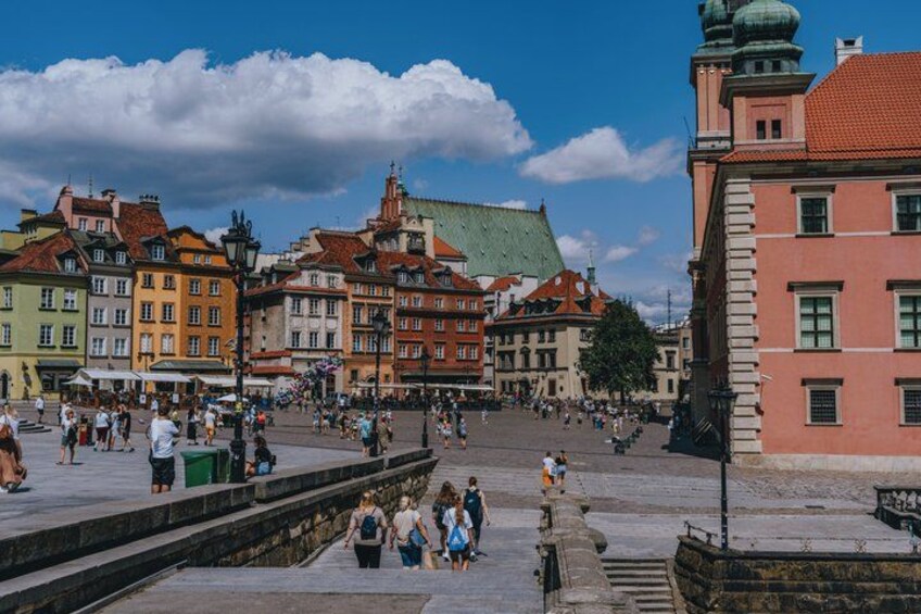 A bustling square with historic buildings, a prominent green-roofed structure, and a stone wall. 5